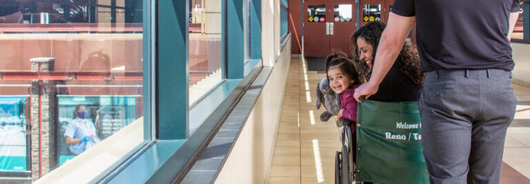 Woman and child being pushed in a wheelchair down the sky bridge.
