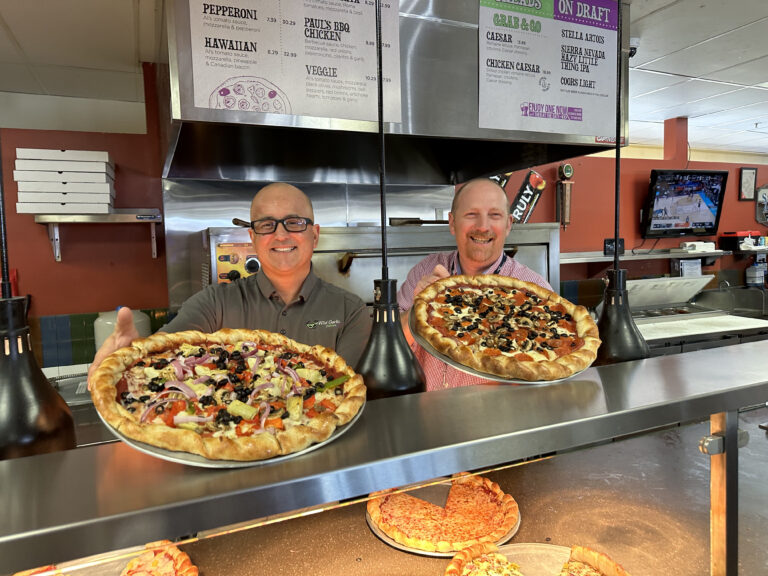 Wild Garlic Pizza owner Dean and Will from SSP (Food Travel Experts America) holding pizzas and posing for a photo.