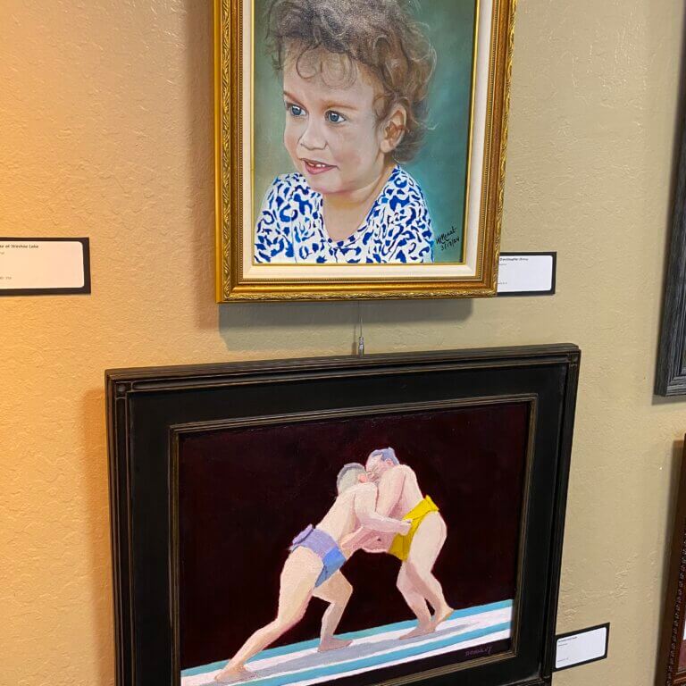 Photo of two framed paintings. One depicts a child and the other depicts two sumo wrestlers.